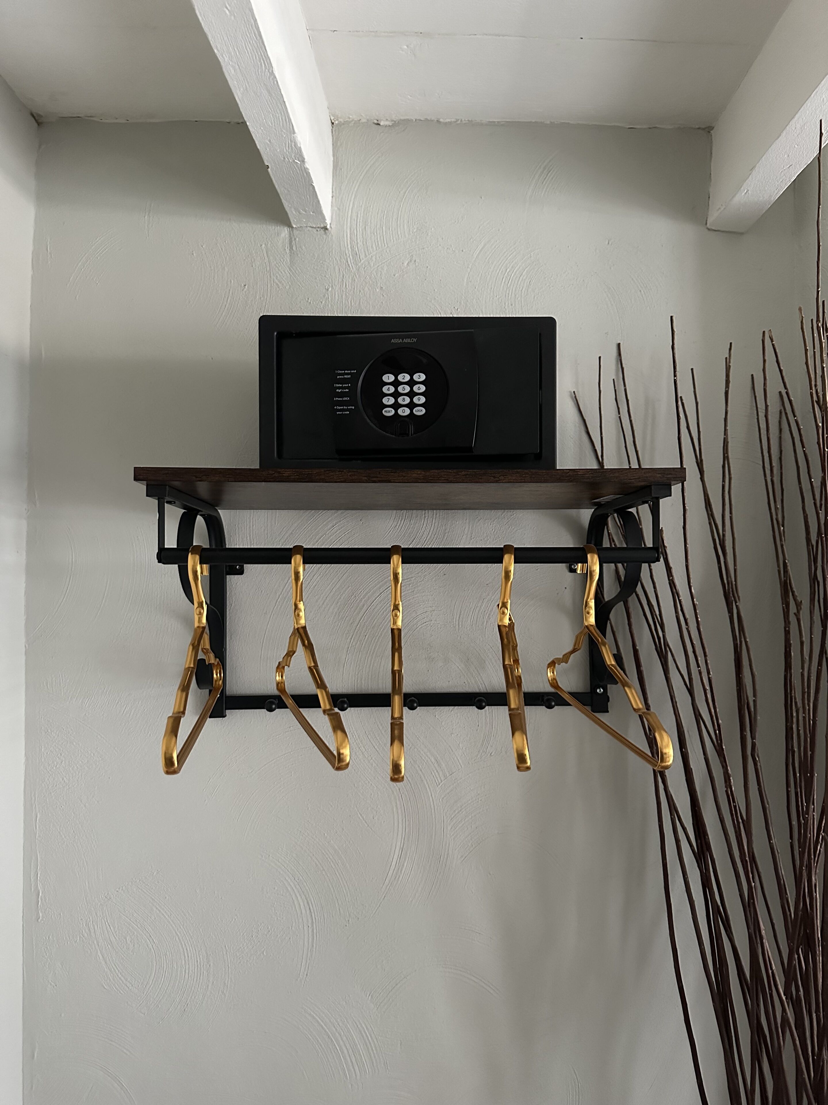 Une étagère murale sur laquelle repose un appareil électronique noir et un porte-manteau en laiton.