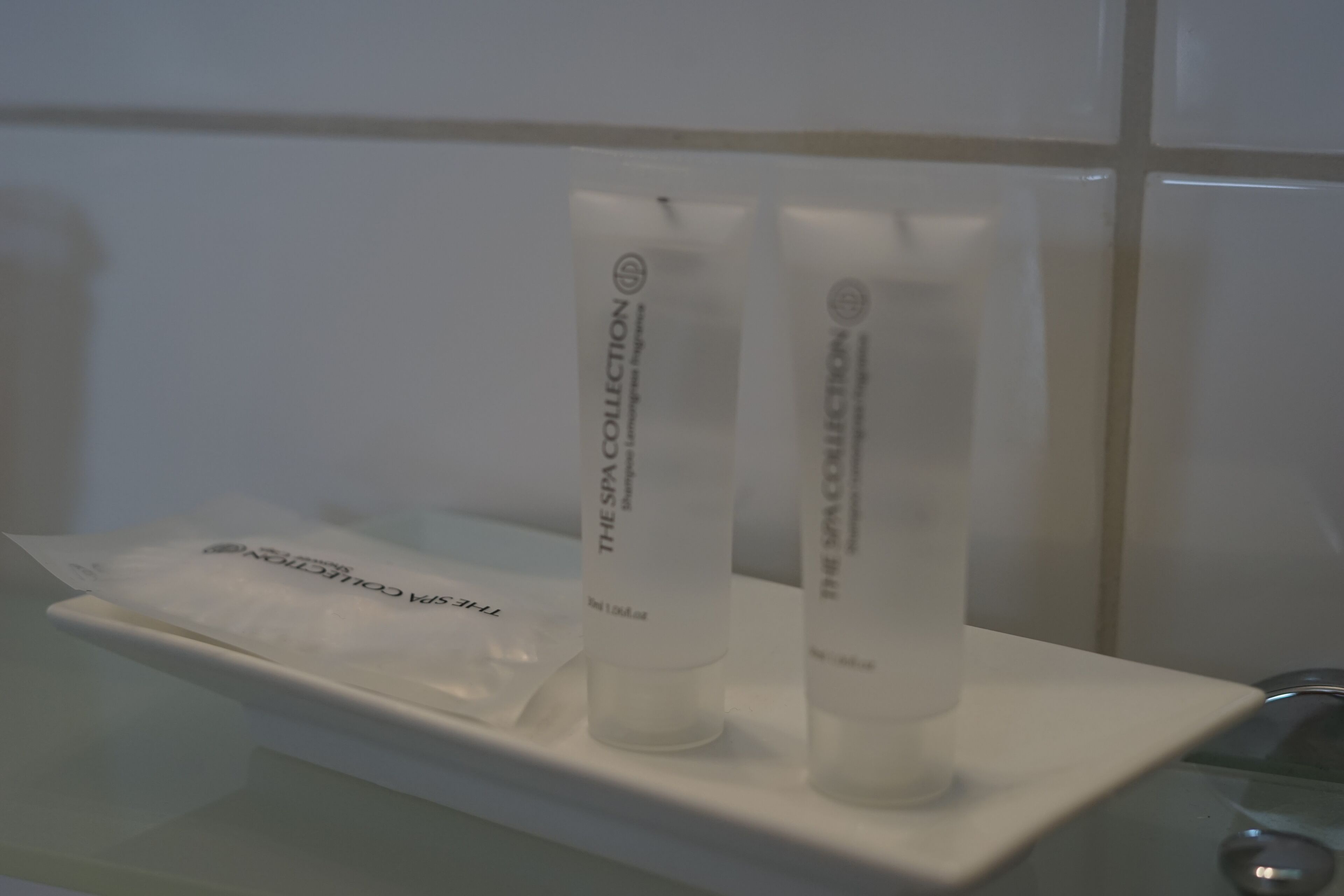 Casa de banho com lavatório branco e duas embalagens brancas com a inscrição "The Spa Collection" numa prateleira branca.