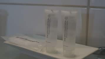 Casa de banho com lavatório branco e duas embalagens brancas com a inscrição "The Spa Collection" numa prateleira branca.