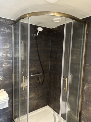 Una ducha con cerramiento de vidrio, cabezal de ducha manual y manguera.