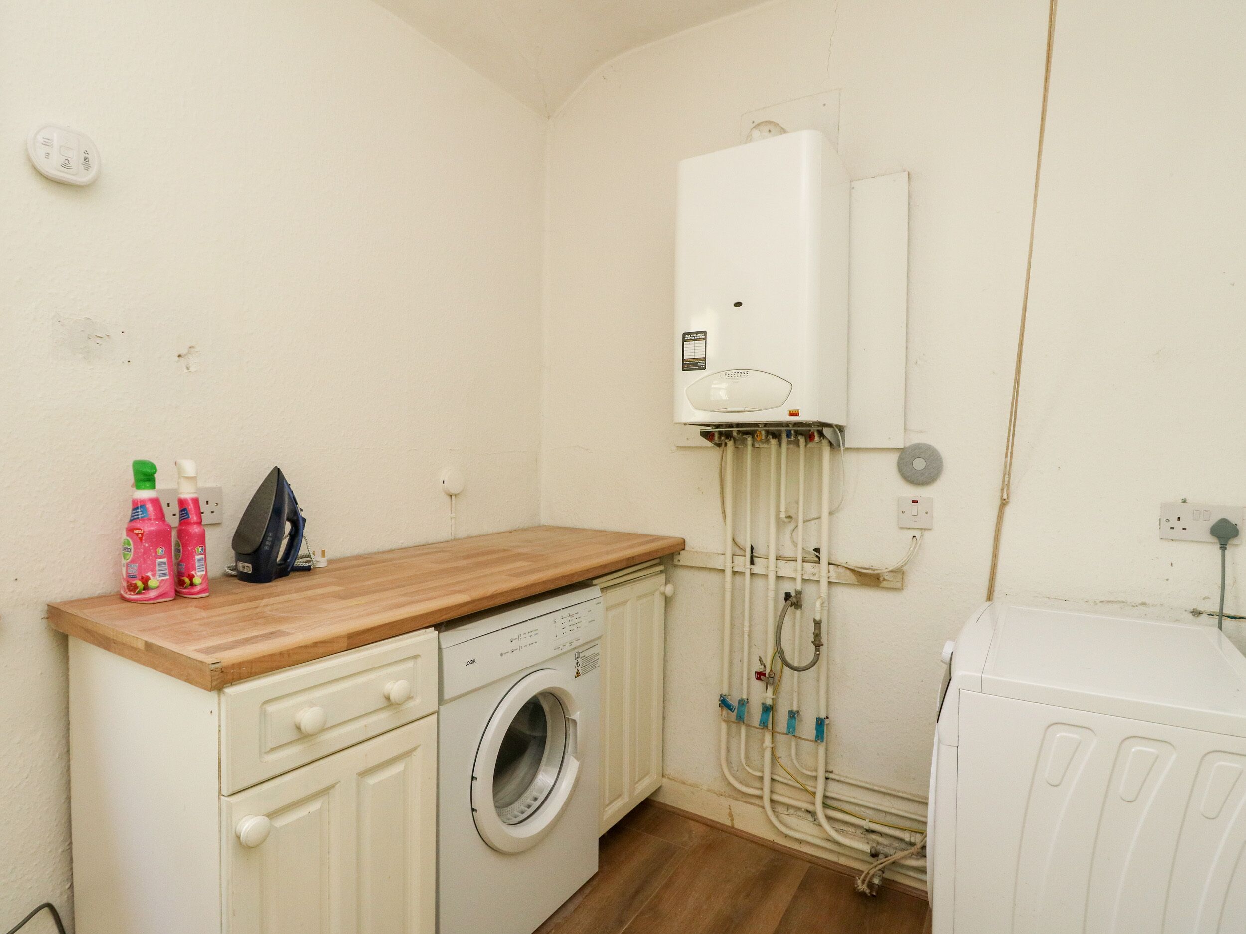 A compact laundry room with a washing machine, a drying rack, and a water heater mounted on the wall.