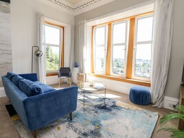 A living room with a blue sofa, a round coffee table, and a view of a cityscape through large windows.
