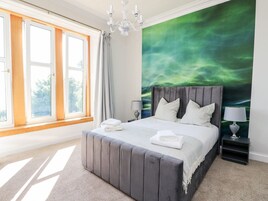 A modern bedroom with a large bed, a view of the outdoors through a window, and a green wall mural.