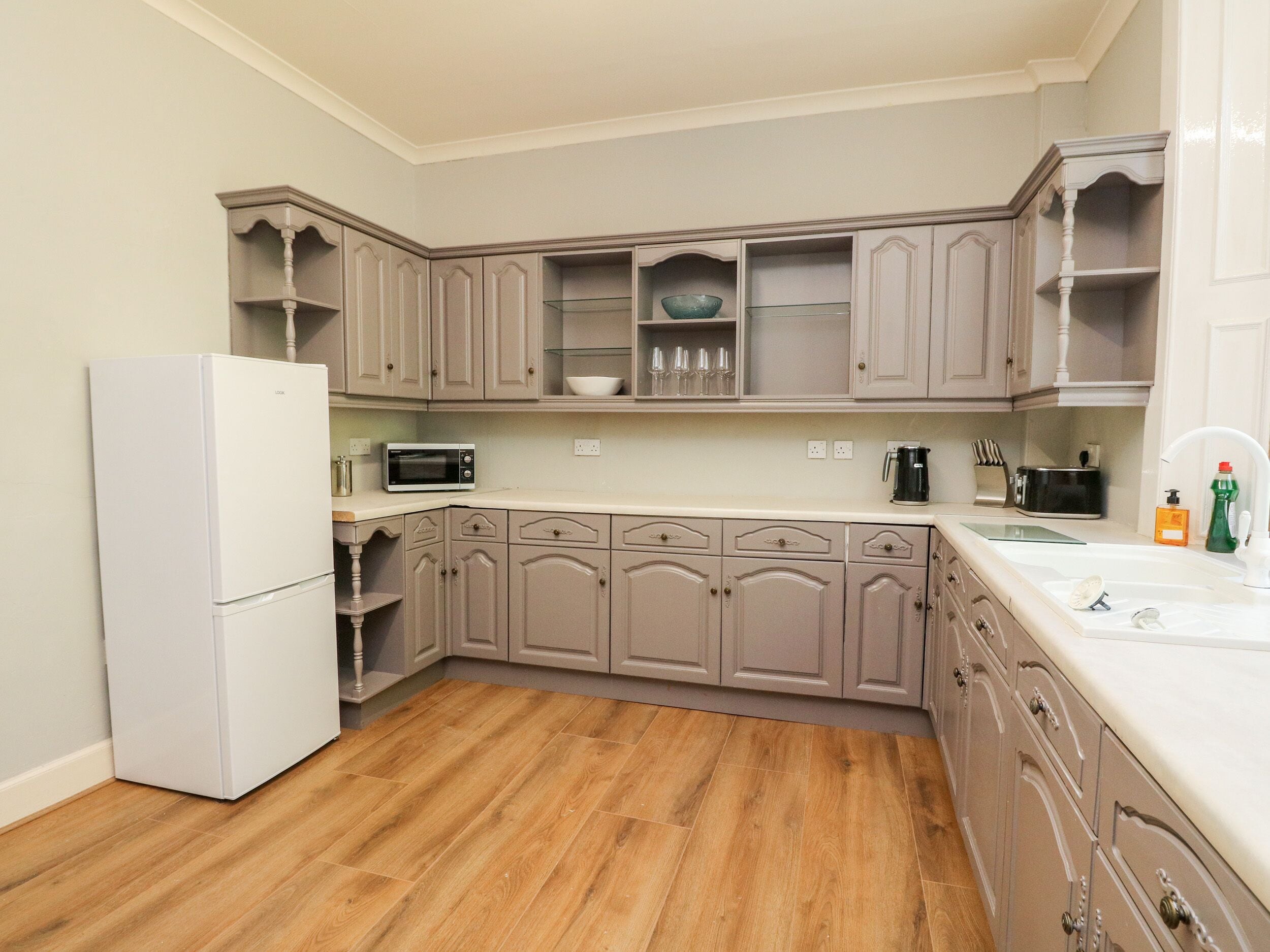 Una cocina con piso de madera, electrodomésticos blancos y gabinetes de colores claros.