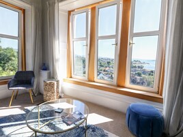 A room with large windows, a chair, a glass table, and a blue ottoman.