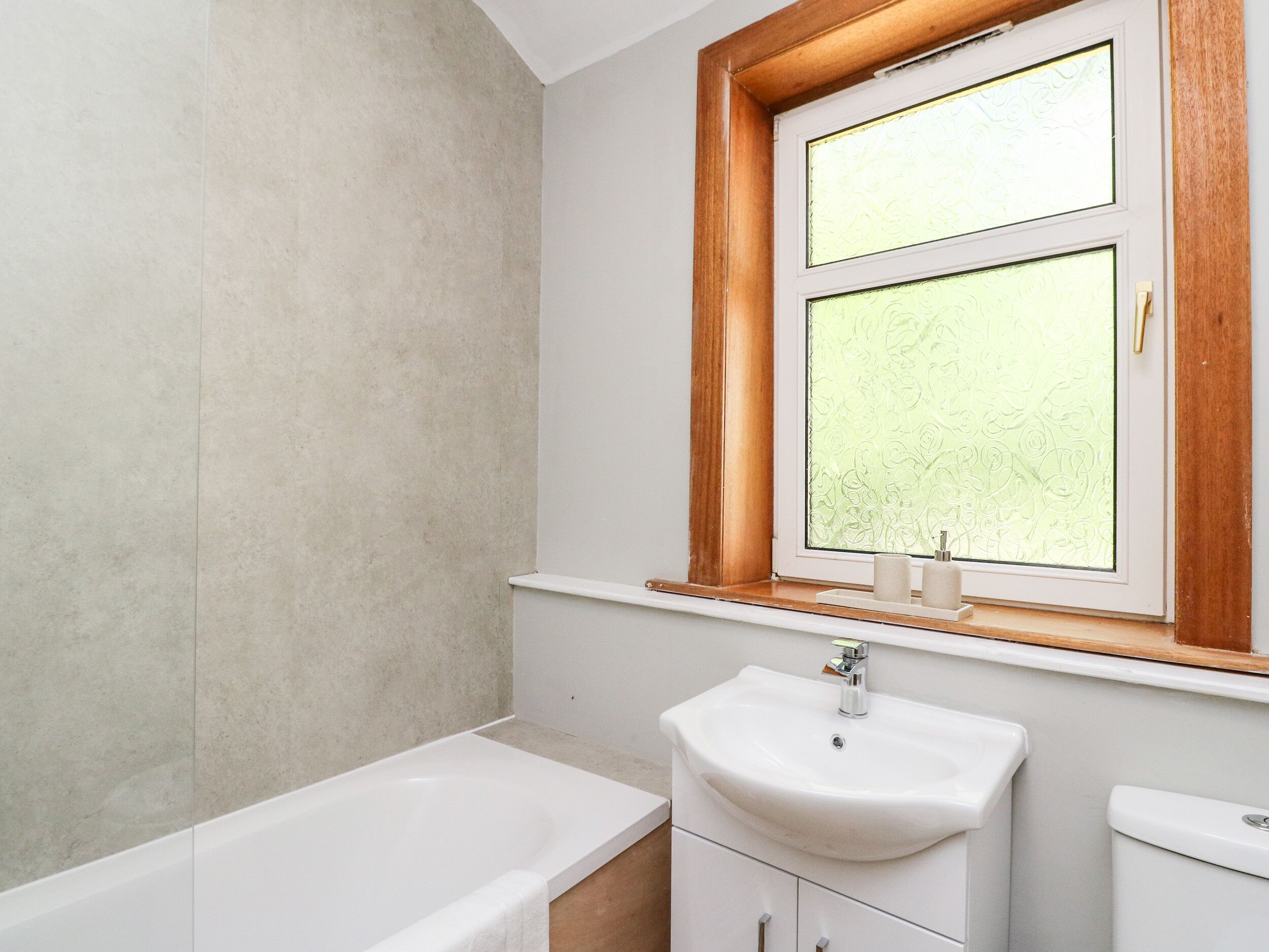 Un baño con bañera, lavamanos y ventana con vidrio esmerilado.