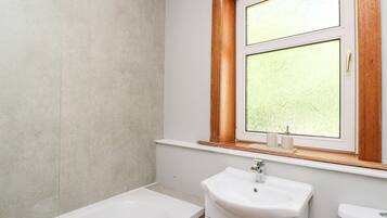 Un baño con bañera, lavamanos y ventana con vidrio esmerilado.