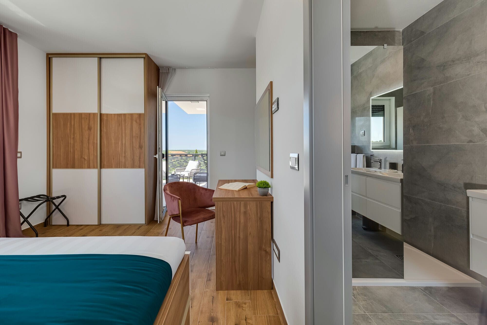 Une chambre d’hôtel moderne, équipée d’un lit, d’un bureau, d’une chaise, d’une petite plante en pot et offrant une vue sur la ville.