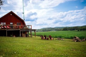 Een rode schuur met een balkon, omgeven door een groen veld en een heldere lucht.