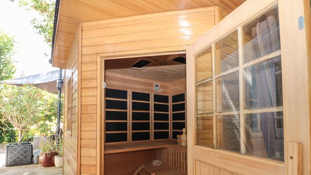 A wooden sauna with a glass door, a wooden bench, and a small table. - The Hideaway (Hove)