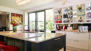 A modern kitchen with a large island, white cabinets, and a glass display cabinet filled with bottles and glassware. - The Hideaway (Hove)