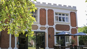 A two-story building with a brick exterior and white trim. There is a patio area with outdoor furniture and a table. - The Hideaway (Hove)