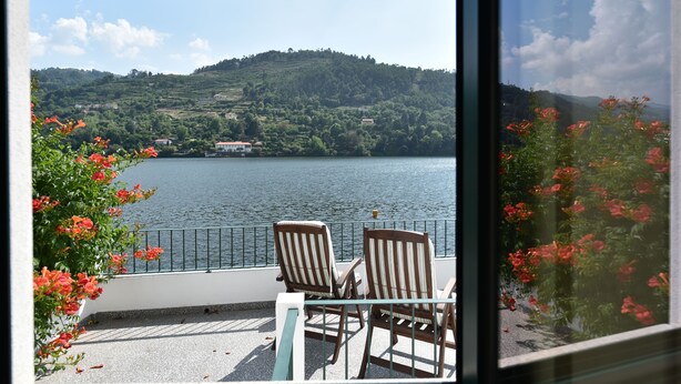 A balcony with two chairs and a table overlooking a lake with hills in the background. - Feel Discovery Casa do Rio Douro Valley (Baiao)