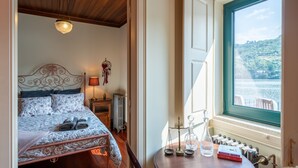 A bedroom with a bed, bedside lamp, and a view of a lake through a window. - Feel Discovery Casa do Rio Douro Valley (Baiao)