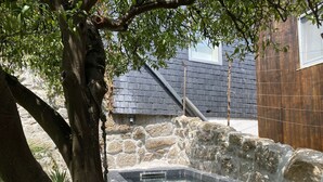 A stone hot tub surrounded by trees, with a stone wall and a building with a grey roof in the background. - Feel Discovery Casa do Rio Douro Valley (Baiao)