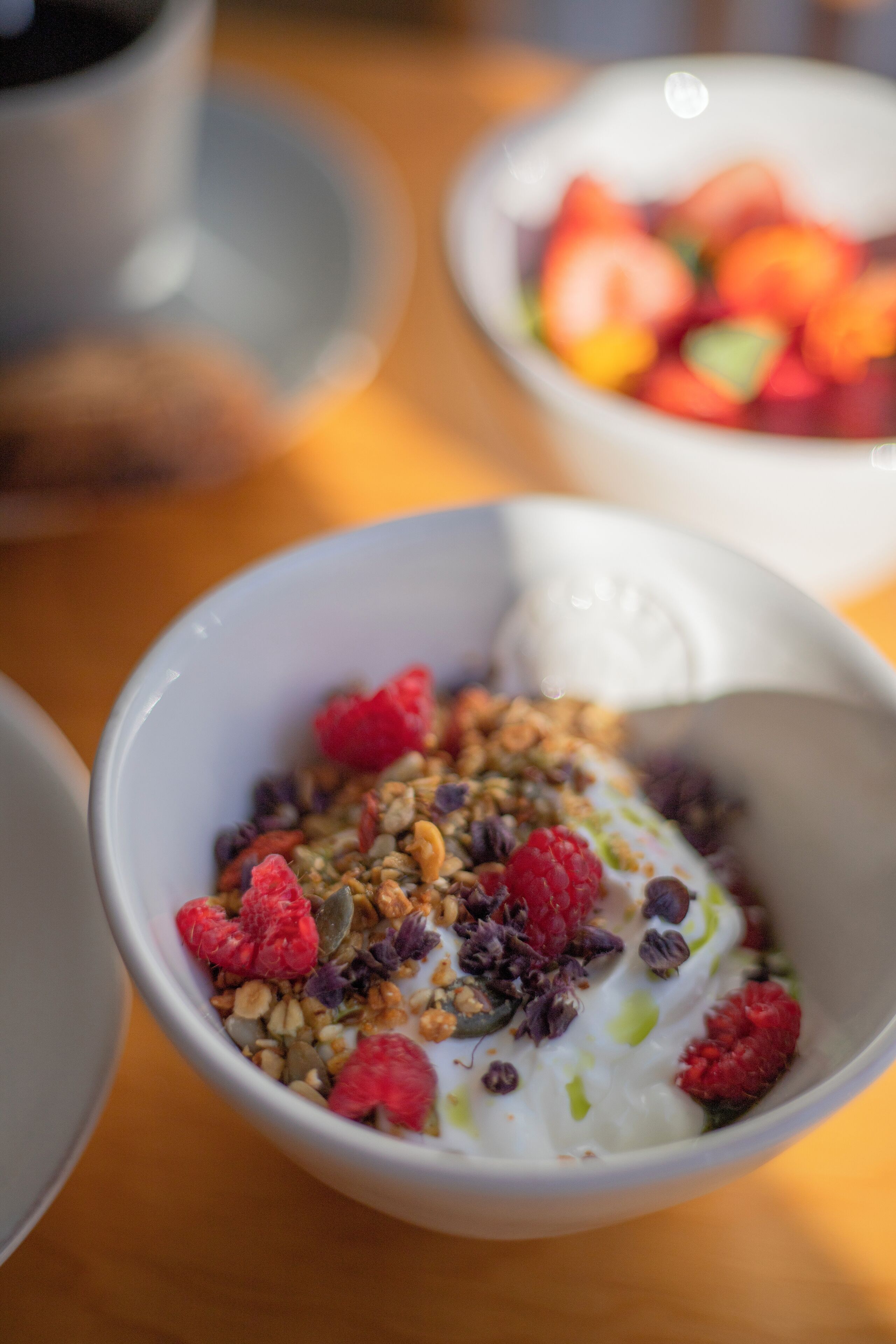 A bowl of yogurt with granola and raspberries on a wooden table.