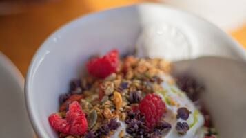 A bowl of yogurt with granola and raspberries on a wooden table.