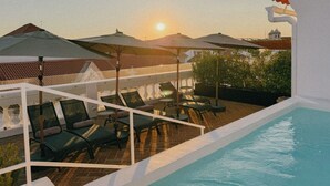 A rooftop pool area with lounge chairs and umbrellas, overlooking a cityscape during sunset. - Casa do Gadanha (Estremoz)