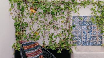 A chair with a colorful cushion, a tiled floor, and a wall with climbing plants and blue decorative tiles.