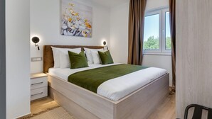 A bedroom with a bed, a nightstand, a wall-mounted light, a window with curtains, and a painting on the wall. - Villa Kate Zadarvillas (Nin)