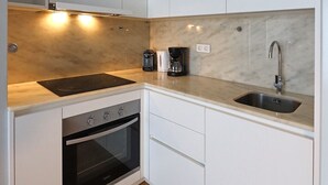 A compact kitchen with white cabinets, a built-in oven, a sink, and a coffee maker. - FLH Boavista Flat I (Oporto)