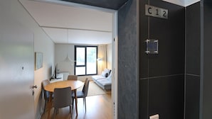 A modern hotel room with a dining area, a sofa, and a large window. - FLH Boavista Flat I (Oporto)