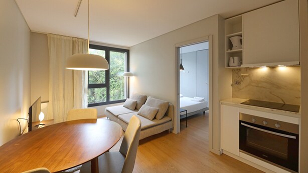 A modern kitchen with a built-in oven and a dining area with a wooden table and chairs. - FLH Boavista Flat II (Oporto)
