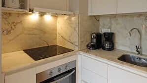 A compact kitchen with white cabinetry, a built-in oven, a stovetop, and a coffee maker. - FLH Boavista Flat II (Oporto)