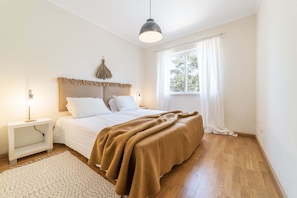Ein Schlafzimmer mit einem Bett, Nachttischen, einer Lampe, einem Fenster mit Vorhängen und einer Hängelampe.