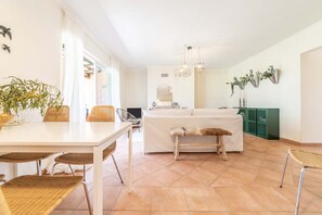 Eine helle Küche mit weißer Arbeitsplatte, Korbstühlen, einer Bank und einem grünen Schrank.