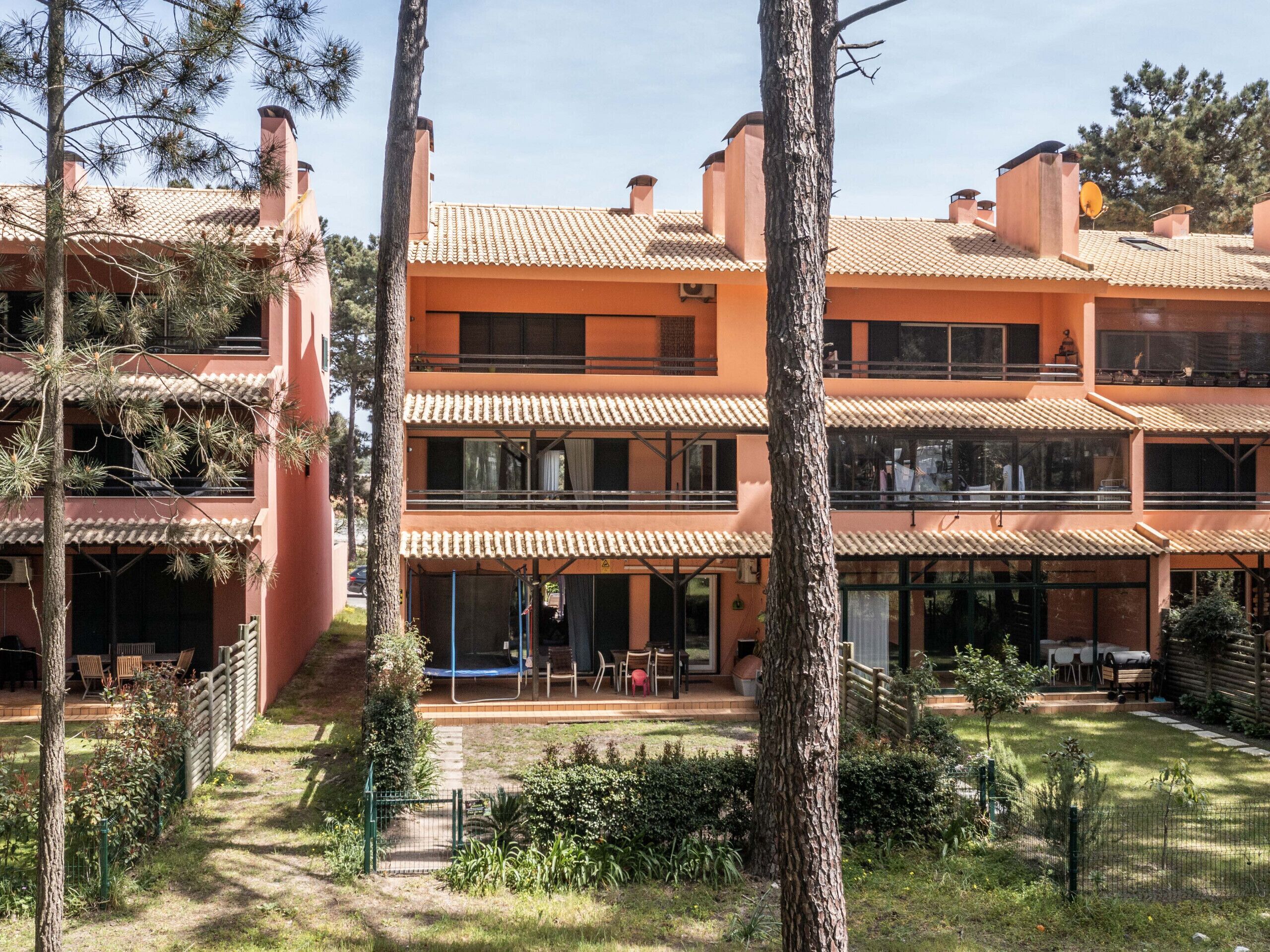 A multi-story building with a tiled roof, balconies, and a courtyard with trees and outdoor seating.