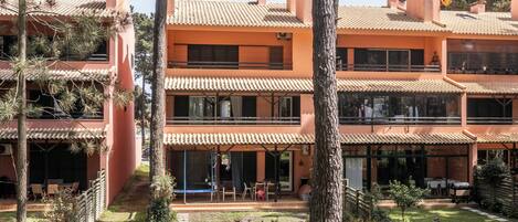 A multi-story building with a tiled roof, balconies, and a courtyard with trees and outdoor seating.