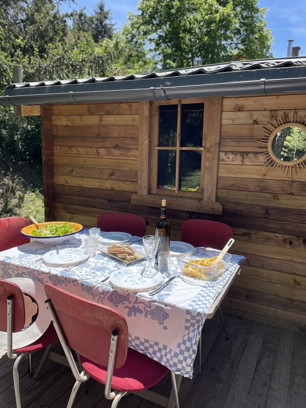 A wooden cabin with a dining table set for two, featuring a checkered tablecloth, plates, cutlery, and a bottle.