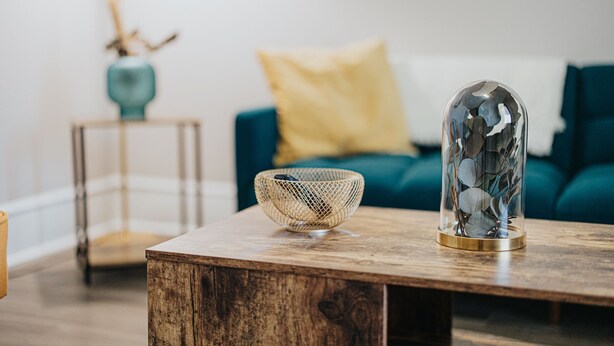 Una mesa de centro de madera con una cúpula de vidrio y un cuenco tejido.