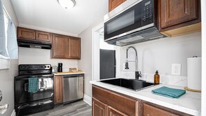 Una cocina con armarios de madera, lavavajillas de acero inoxidable, estufa negra, microondas y un lavabo con grifo.