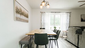 A modern living room with a dining area, featuring a wooden dining table, green upholstered chairs, a grey sofa, and a small side table.