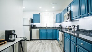 A modern kitchen with blue cabinets, a stainless steel refrigerator, a coffee maker, and a microwave.