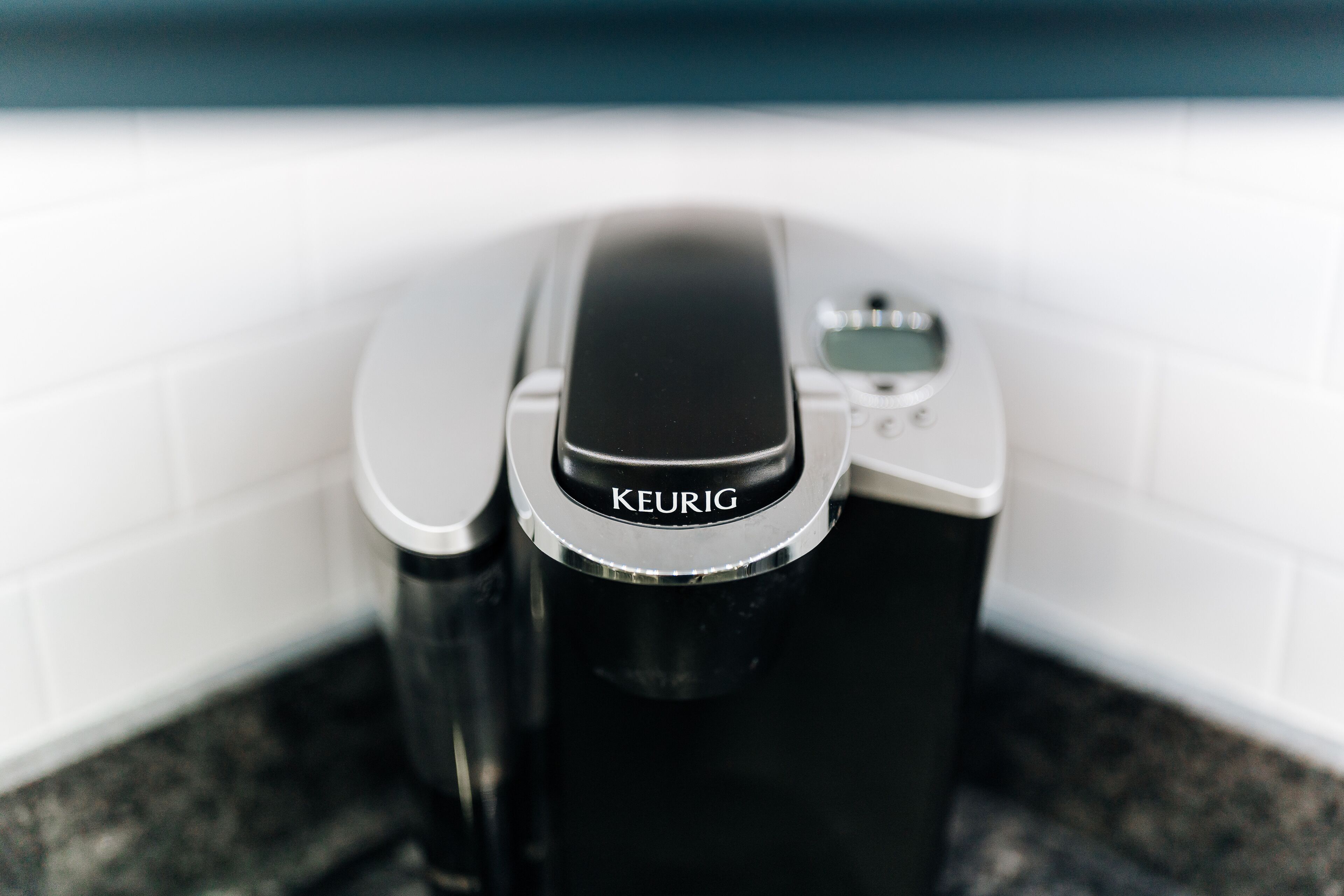 A Keurig coffee maker on a countertop with a white tiled backsplash.