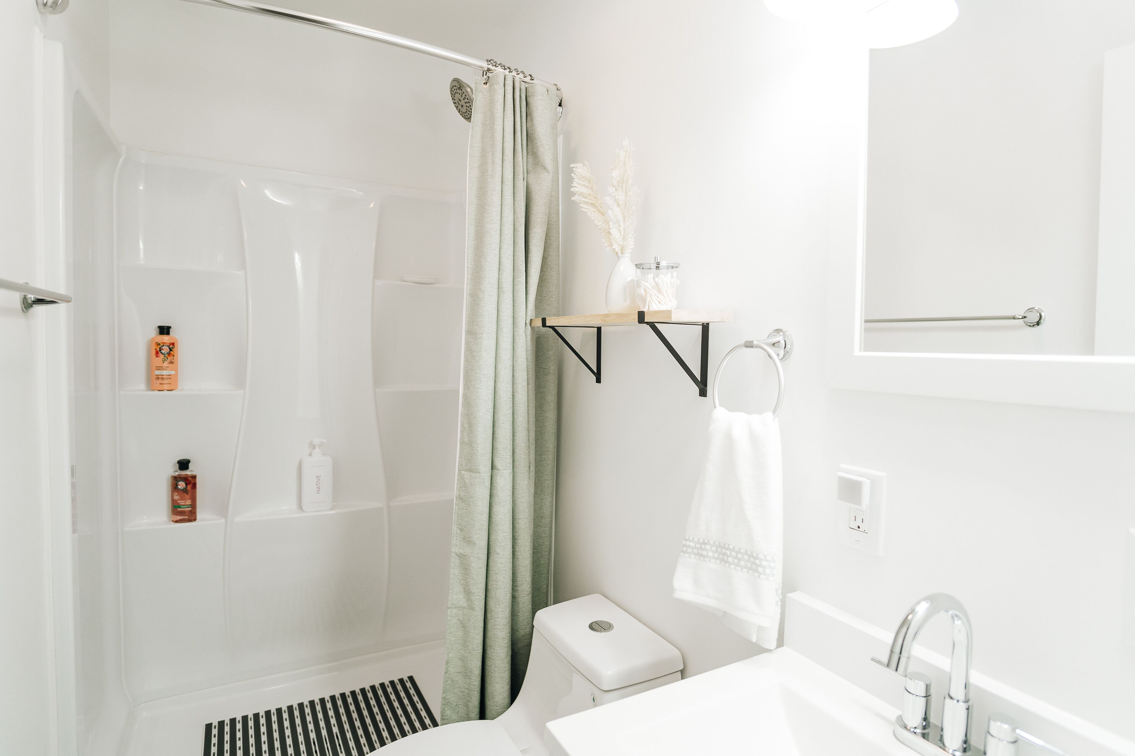 A bathroom with a shower, toilet, sink, and mirror.