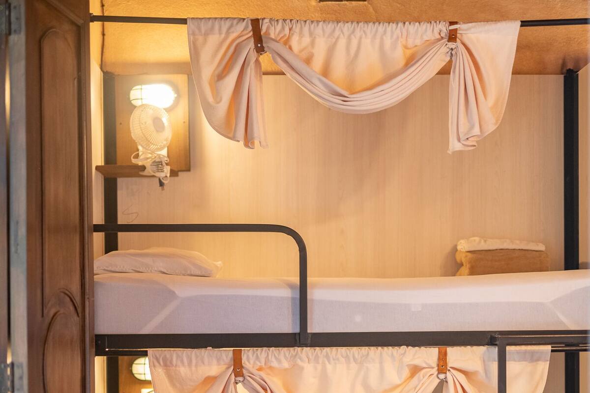 A bunk bed room with a wooden wardrobe, a wall-mounted fan, and a light fixture.