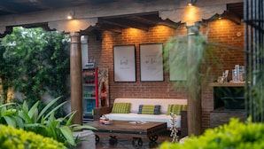 An outdoor seating area with a wooden table, a sofa with cushions, and framed quotes on the wall.