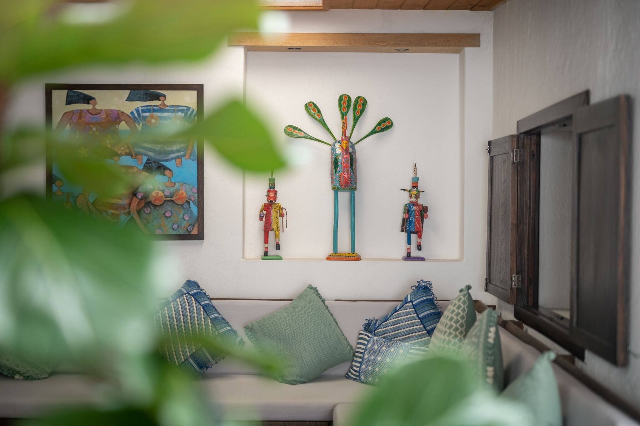 Une pièce avec un mur blanc, un plafond en bois, un canapé agrémenté de coussins à motifs et une œuvre d’art encadrée au-dessus du canapé.