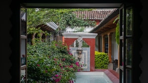 A traditional courtyard with a tiled gate, lush greenery, and a tiled pathway.