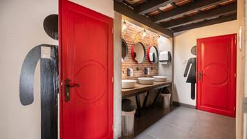 A modern bathroom with red doors, a brick wall, and a wooden ceiling.