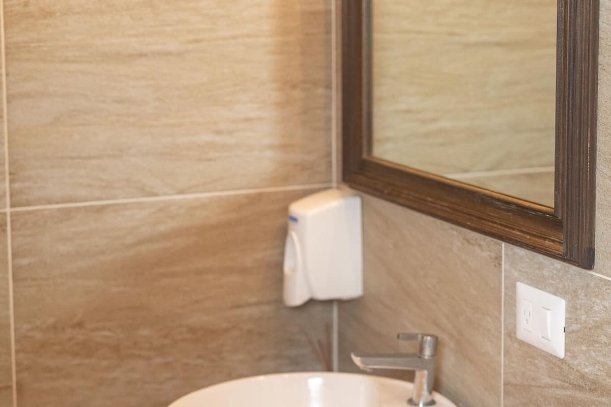 A bathroom with a round white sink, a wooden countertop, a towel rack, and a toilet paper holder.