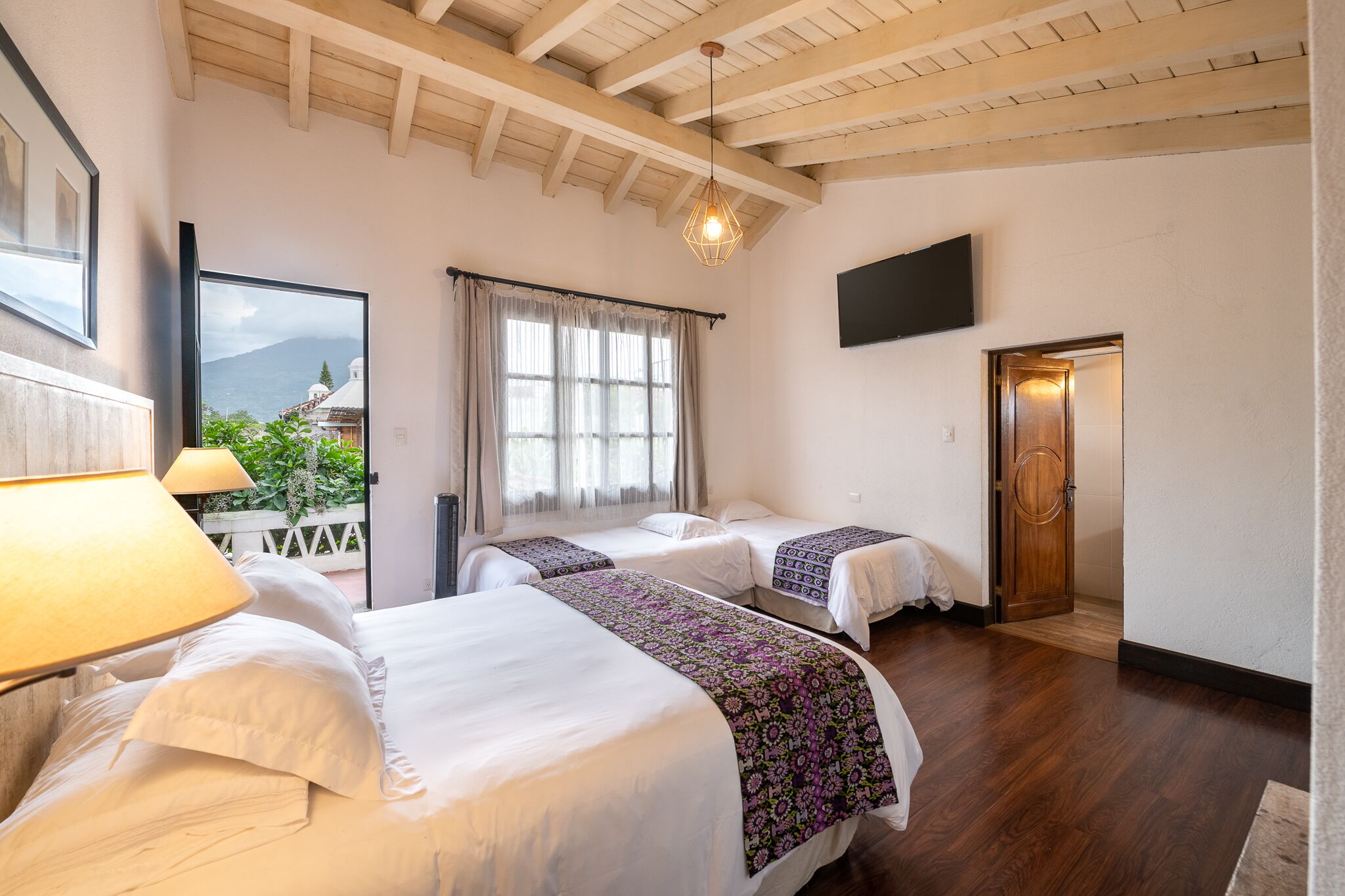 A hotel room with two beds, a TV mounted on the wall, and a wooden ceiling.