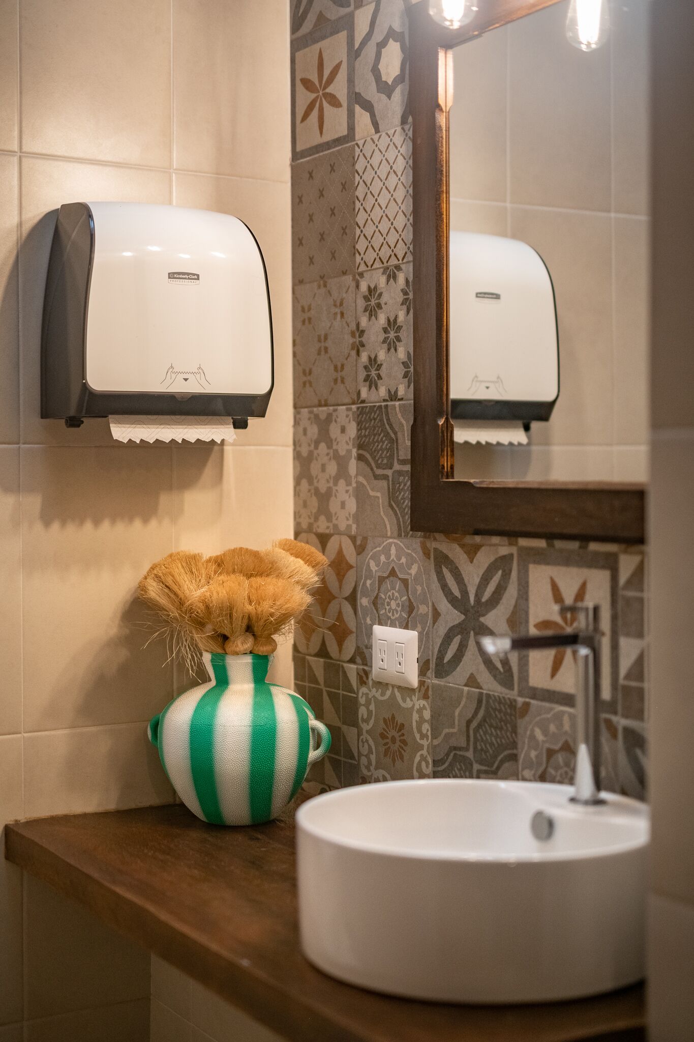 Un bany amb un assecador de mans, un vas verd i blanc a ratlles, i un lavabo.