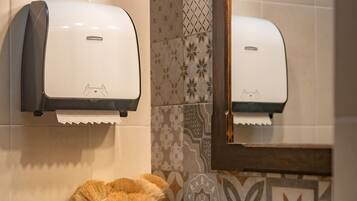 Un bany amb un assecador de mans, un vas verd i blanc a ratlles, i un lavabo.
