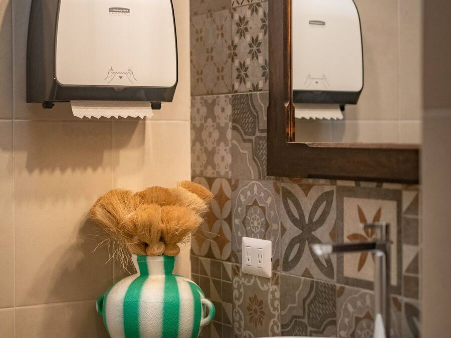 Un bany amb un assecador de mans, un vas verd i blanc a ratlles, i un lavabo.