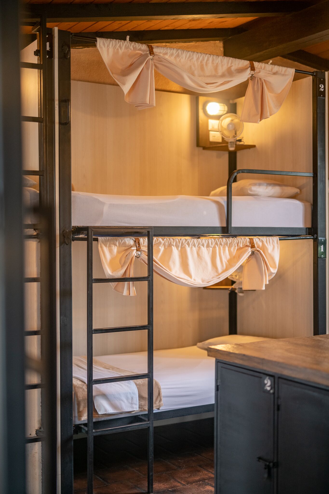 Une chambre avec un lit superposé, une échelle, une table de chevet et un luminaire fixé au mur.